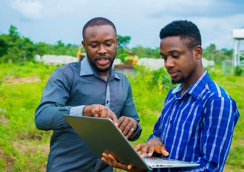 Two young man in a field with a laptop in their hands.